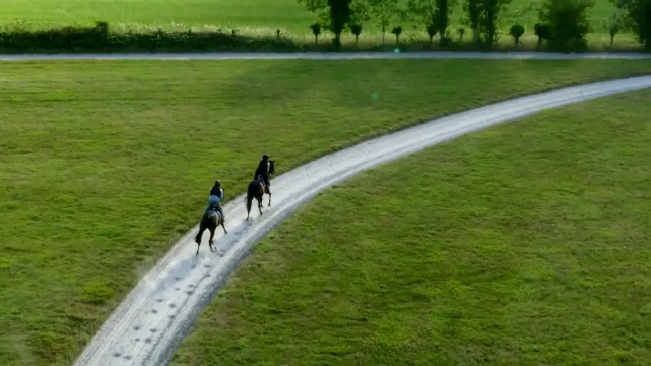 Two racehorses and their riders cantering round the curve of Danebury's all-weather gallop