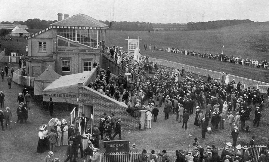 Black-and-white photograph of a crowd in Victorian dress in front of the Stockbridge Racecourse grandstand on race day